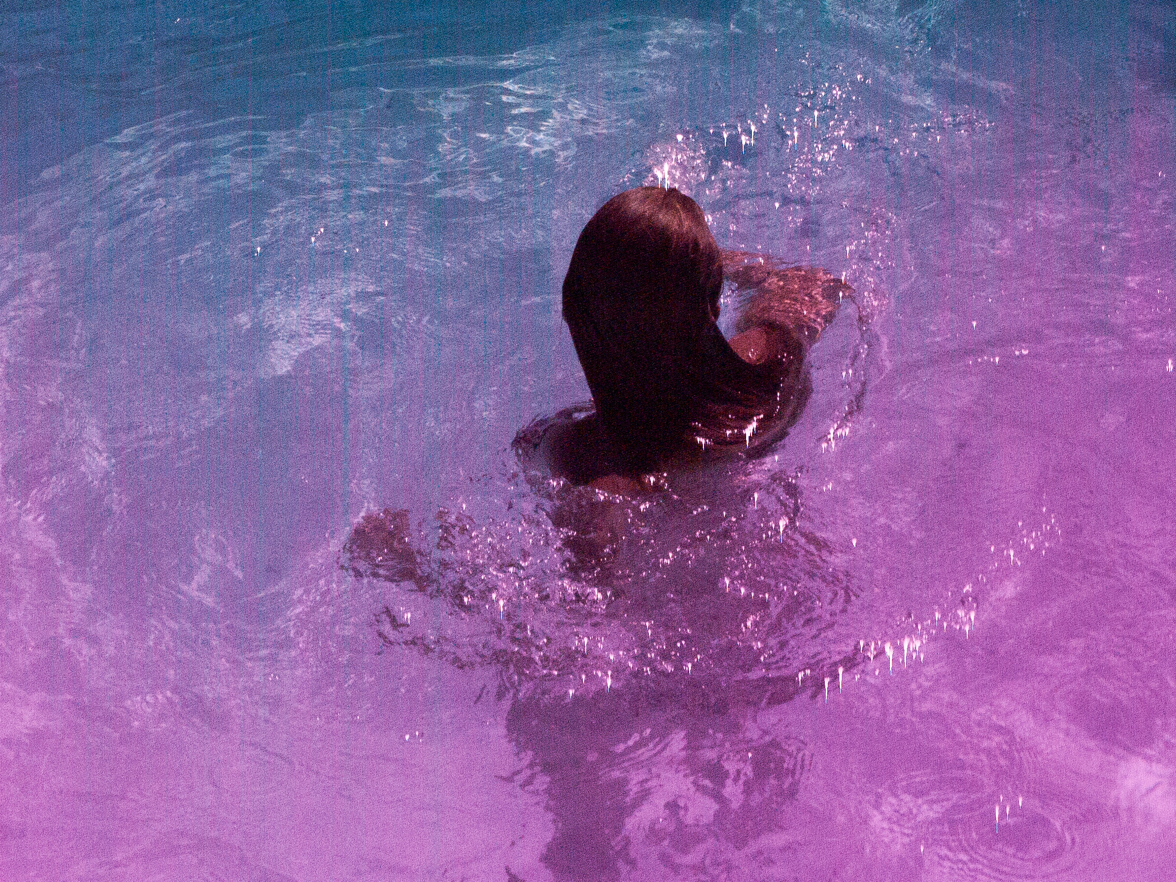 A swimmer seen from above, the pool water shifting from cyan to magenta