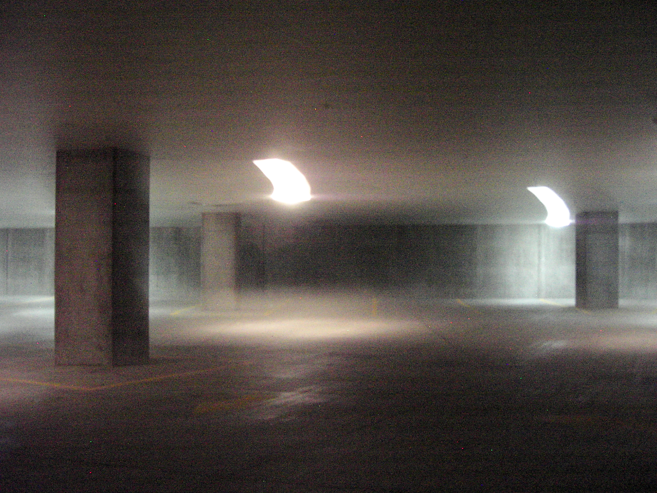 An empty concrete parking garage, columns and ceiling lights smeared by a long handheld exposure into streaks of light
