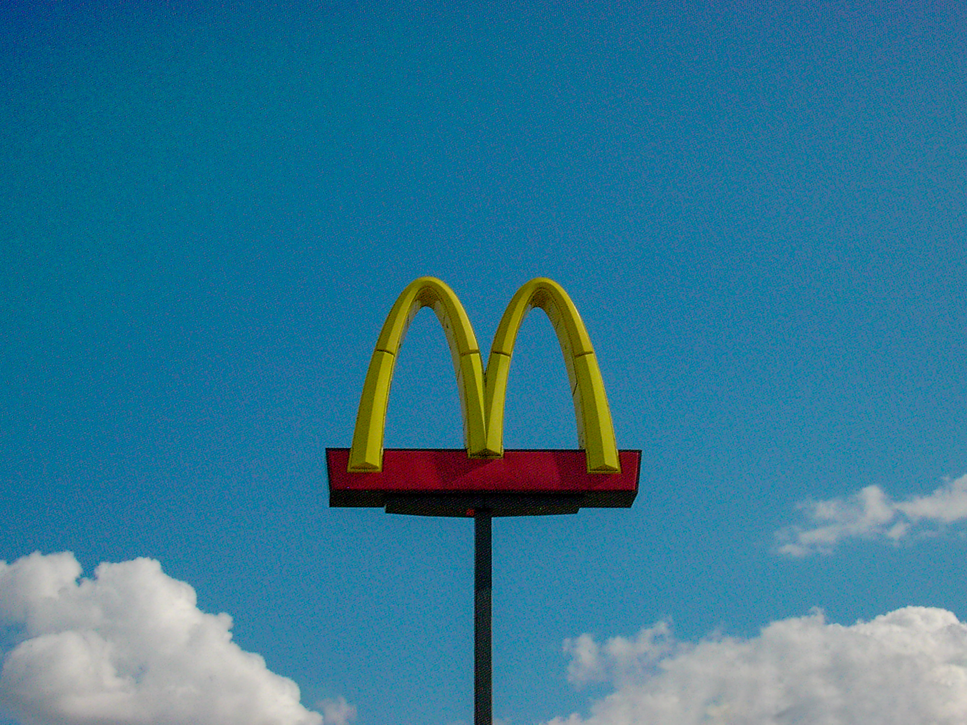 A McDonald's sign floating against a deep blue sky and bright white clouds
